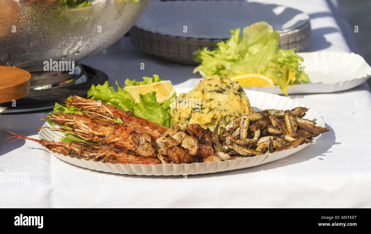 The street food market, seafood served on the paper tray. The green lettuce, kalamari, shrimps, small fried fish (grundle/ Grundeln), mashed potatoes. Stock Photo