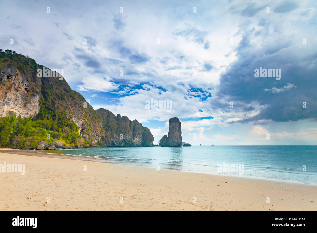 Stunning scene the limestone cliffs covered with the vegetation and the ocean shore on the cloudy sky background. Beauty of wild virgin Thai nature. Ideal place for the calm rest. Stock Photo