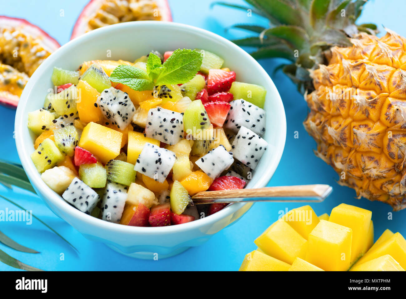 Fruit salad in bowl on blue background. Exotic tropical fruit salad. Dragon fruit, passion fruit, mango, coconut, strawberry and pineapple salad in a  Stock Photo