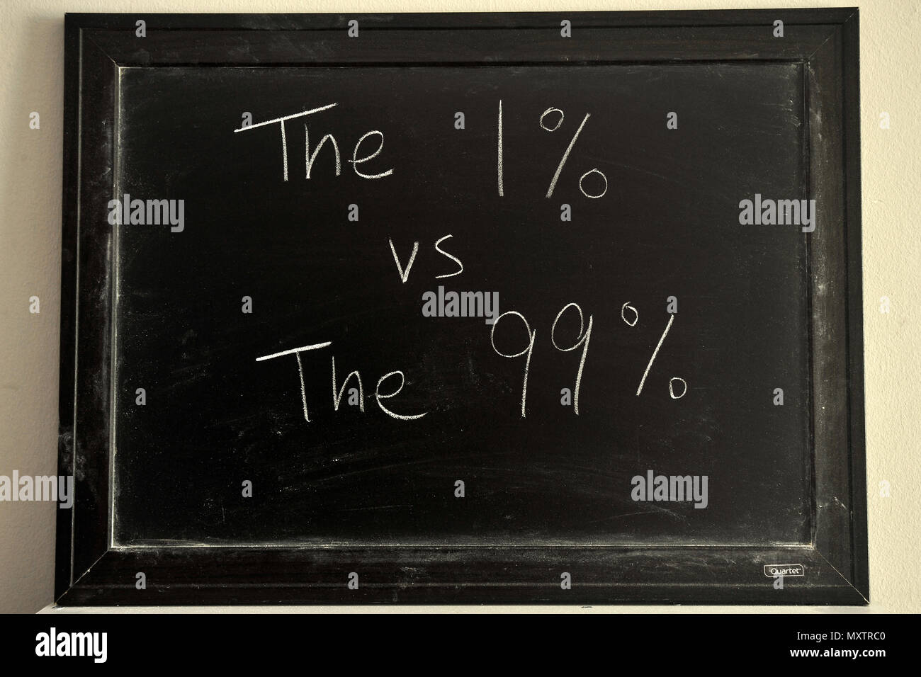The 1% vs The 99% written in white chalk on a blackboard. Stock Photo