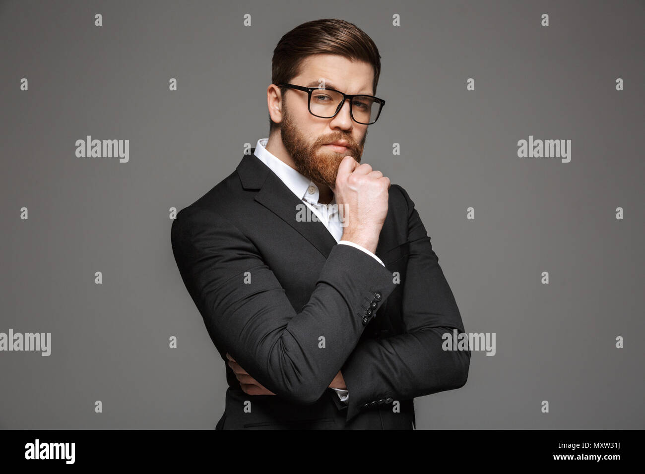 Portrait of a pensive young businessman dressed in suit and eyeglasses ...