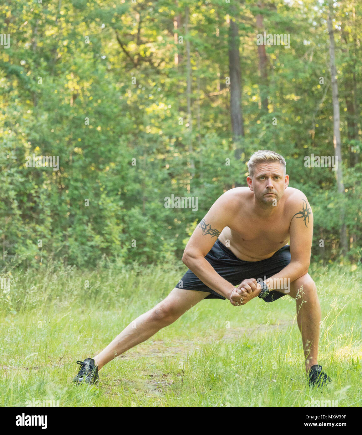 Barechested mid adult 40s caucasian man doing leg stretches before exercising Stock Photo