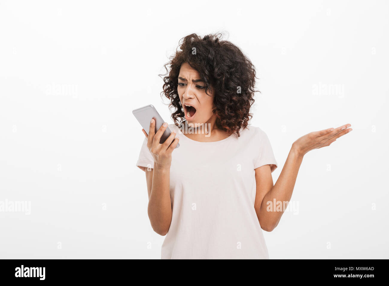 Portrait of american woman with afro hairstyle wearing t-shirt shouting into mobile phone being annoyed and angry isolated over white background Stock Photo