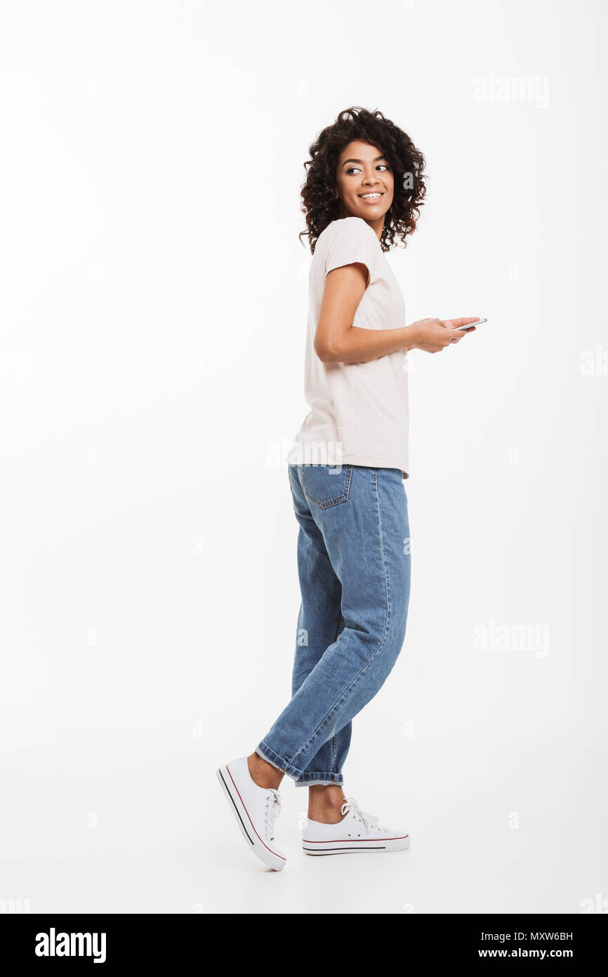 Full length photo of attractive brunette woman with afro hairstyle wearing  t-shirt and jeans using smartphone and looking back isolated over white bac  Stock Photo - Alamy