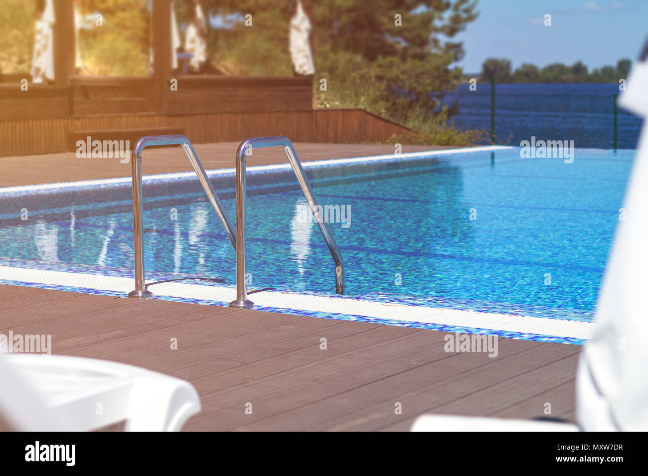 Swimming pool with stair and wooden deck at hotel. Grab bars ladder in ...