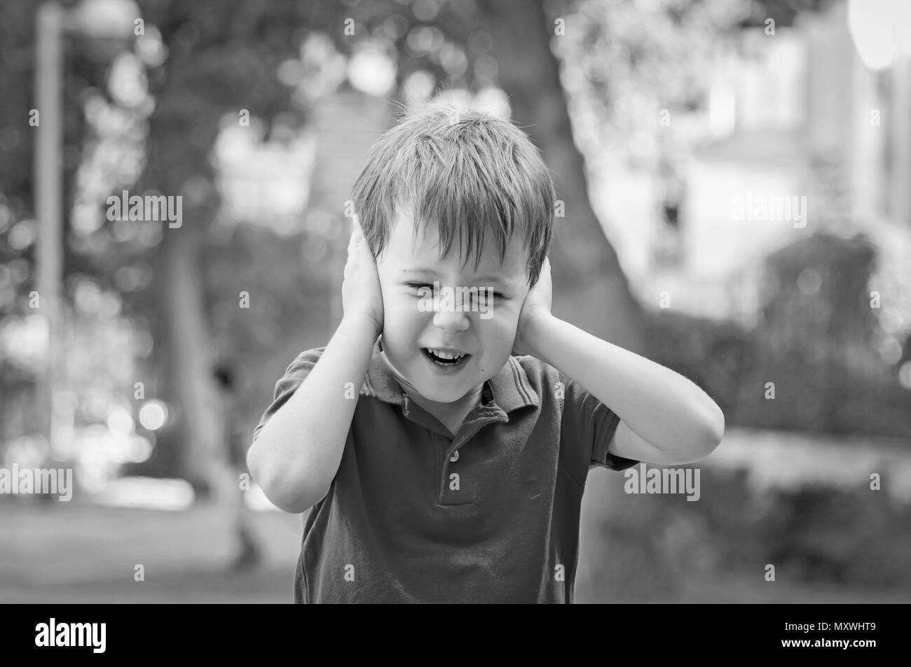 Stressed out little 5-year old Caucasian little boy outside closing his ears and screaming of pain, trauma, traumatic experience and loud noise stock Stock Photo