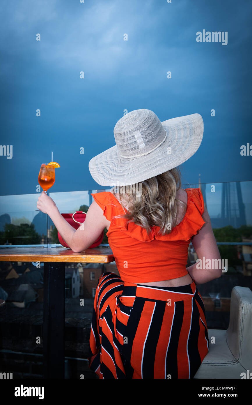 Fashion and lifestyle blogger Andreea Rasclescu at the rooftop bar in Oxford, the Varsity Club, drinking an orange glass of Aperol to match her outfit Stock Photo