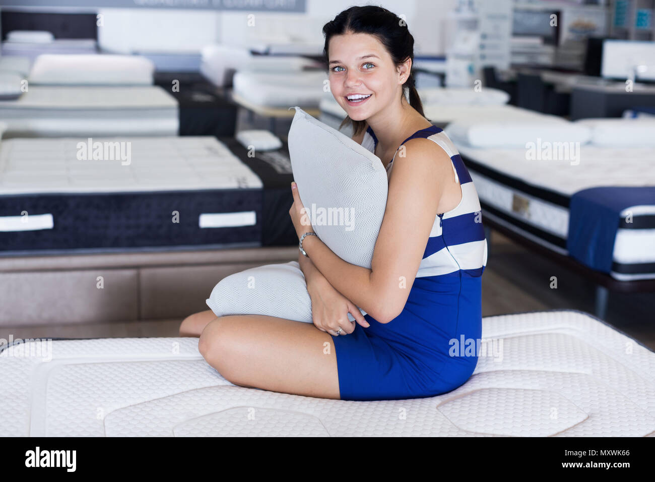 Customer Girl Is Sitting With Pillow And Testing New Mattress