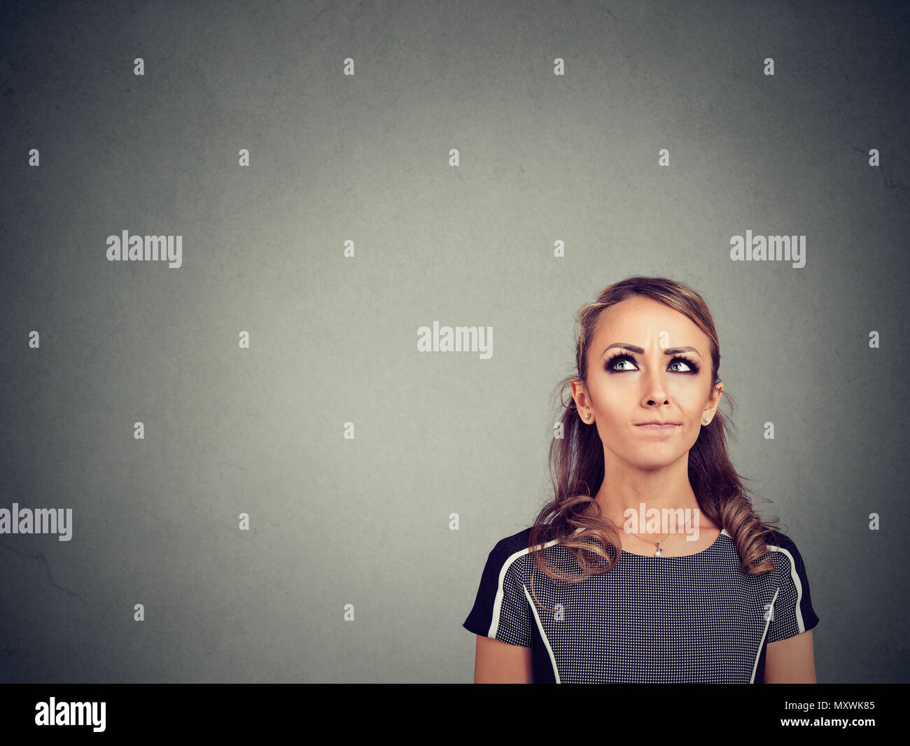 Pretty young woman looking up in suspicion trying to make correct decision Stock Photo