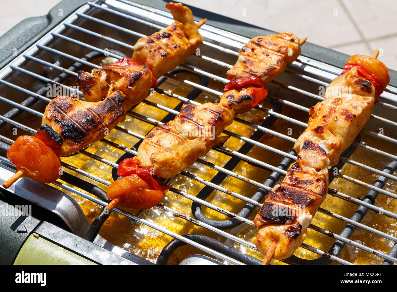 Marinated chicken brochette with pepper and dry apricot on the grid of an electric barbecue Stock Photo