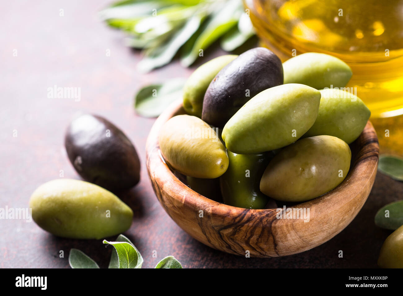 Black and green olives in a bowl and olive oil bottle on dark stone ...