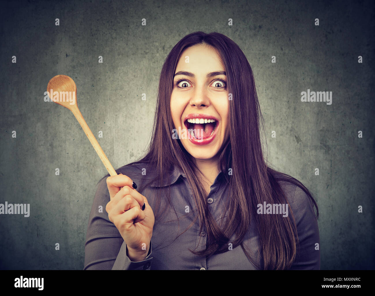 Young woman looking crazily at camera with funny expression of mad housewife and holding wooden spoon Stock Photo
