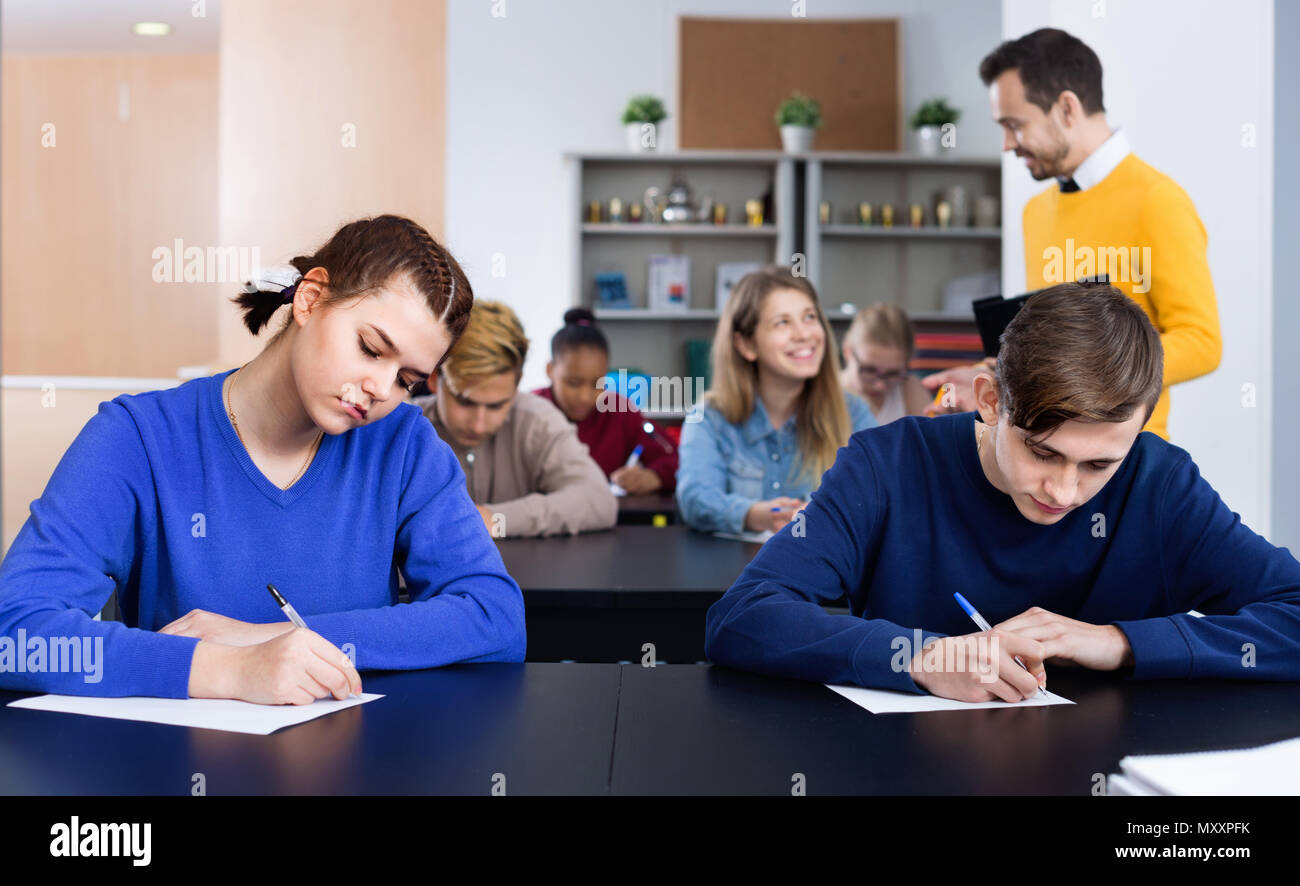 Smiling teacher monitoring students’ work during examination test in class Stock Photo