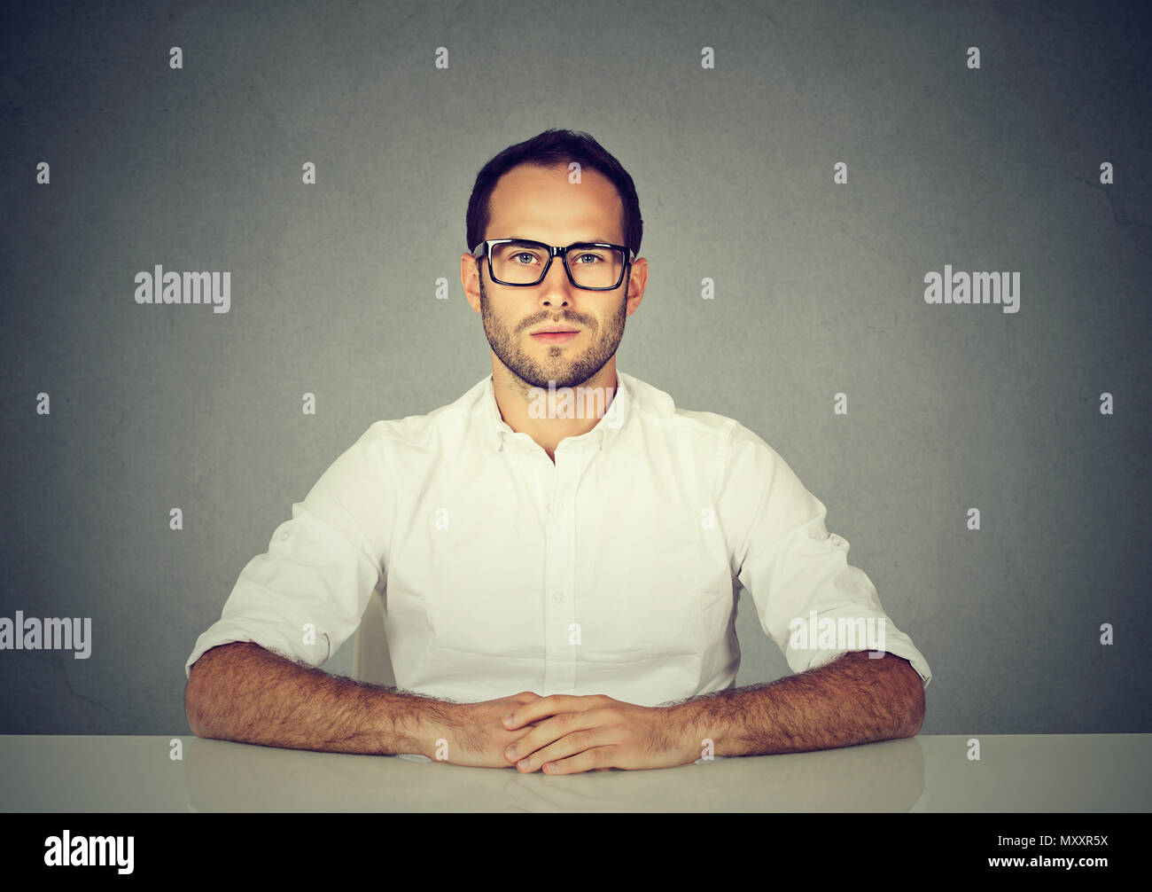 Handsome man wearing white shirt and elegant glasses sitting at table looking highly qualified employee Stock Photo