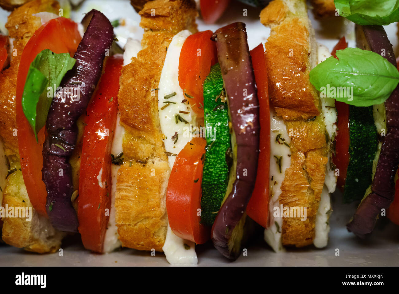 Flat lay top view of oven baked sliced vegetables (tomatoes, aubergines and courgettes) with mozzarella cheese and baguette slices dressed with basil. Stock Photo