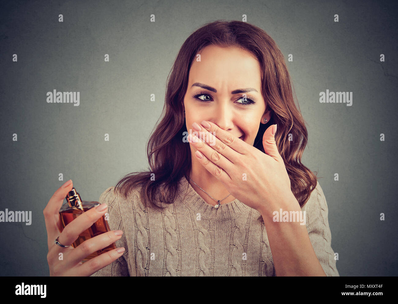 Young woman disgusted with unpleasant stinky perfume holding nose. Stock Photo