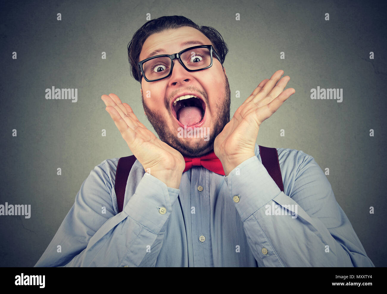 Chunky stylish man in glasses screaming in deep surprise and happy excitement looking at camera on gray Stock Photo