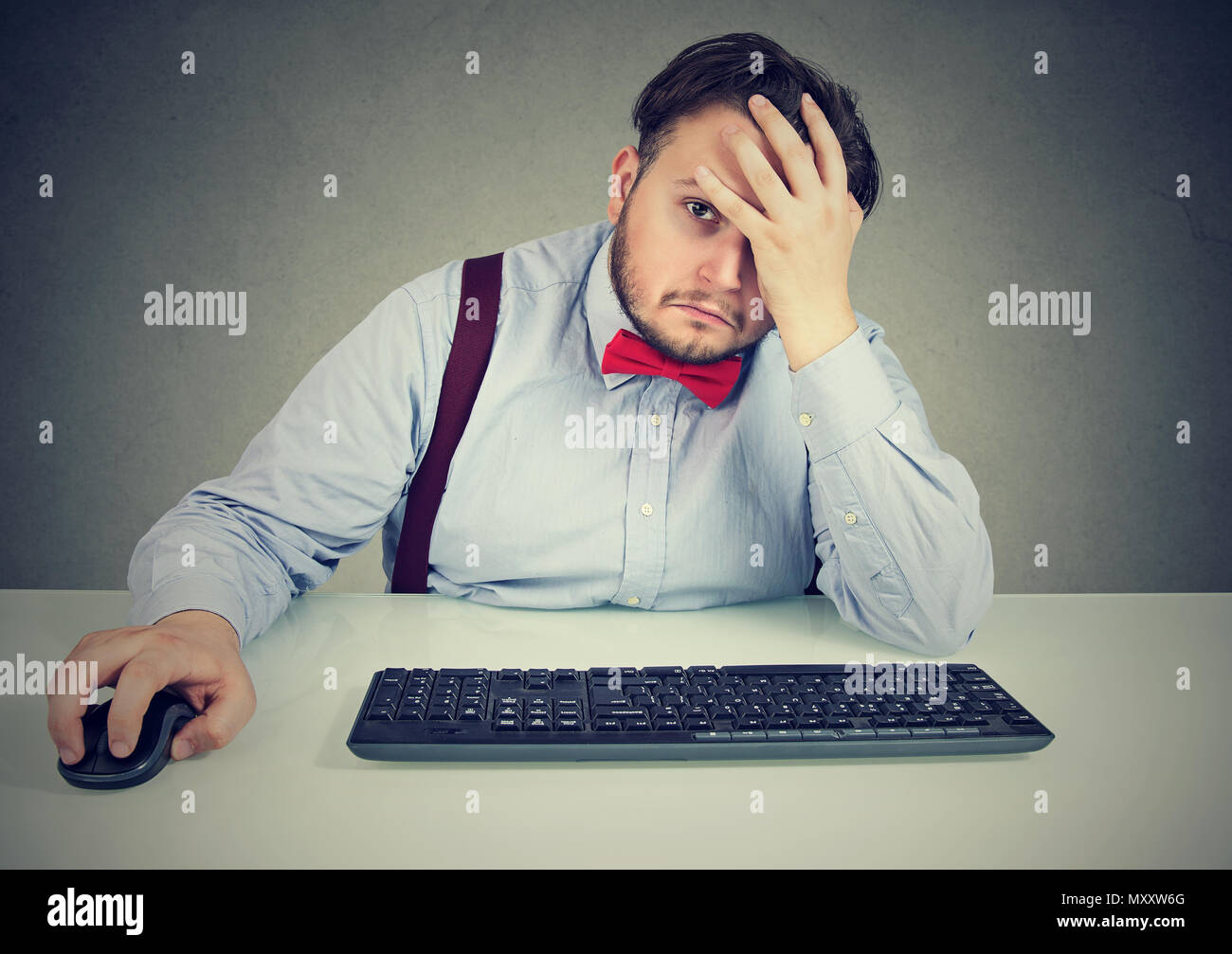 Chunky man at working table leaning on hand in tiredness and looking at camera in stress and fatigue Stock Photo