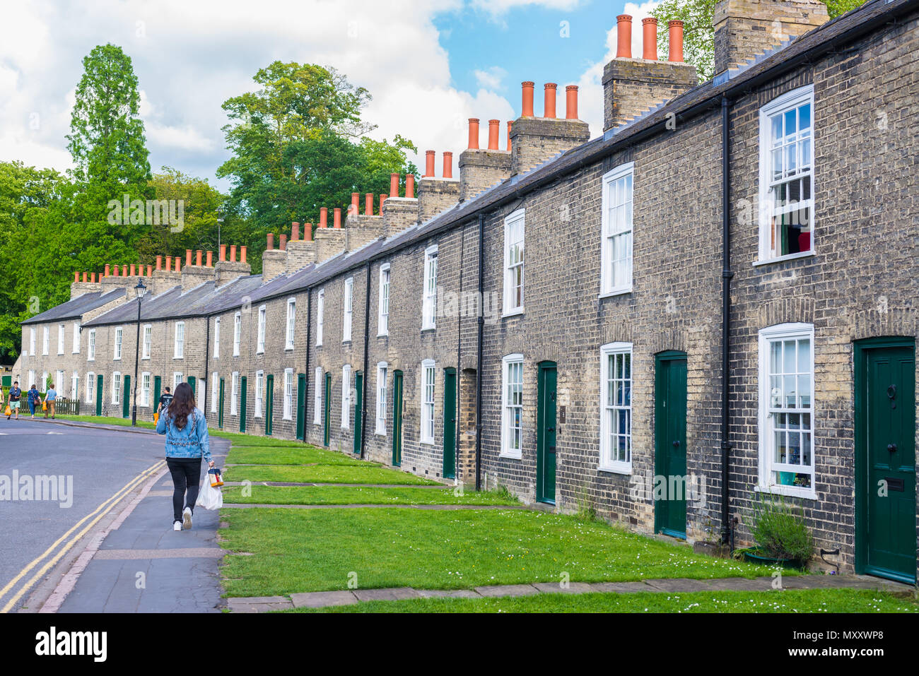 Cambridge, England, UK - June 2018: Row of restored Victorian brick houses with green colored doors on a local road in Cambridge with people walking a Stock Photo