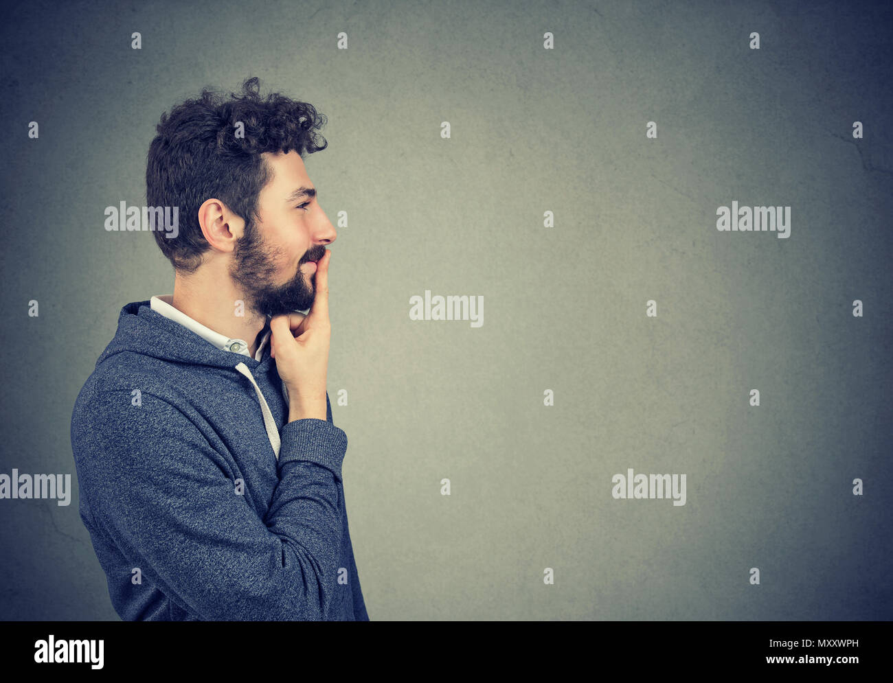 Side view of young hipster man touching lips and looking away in brainstorming while making decision. Stock Photo