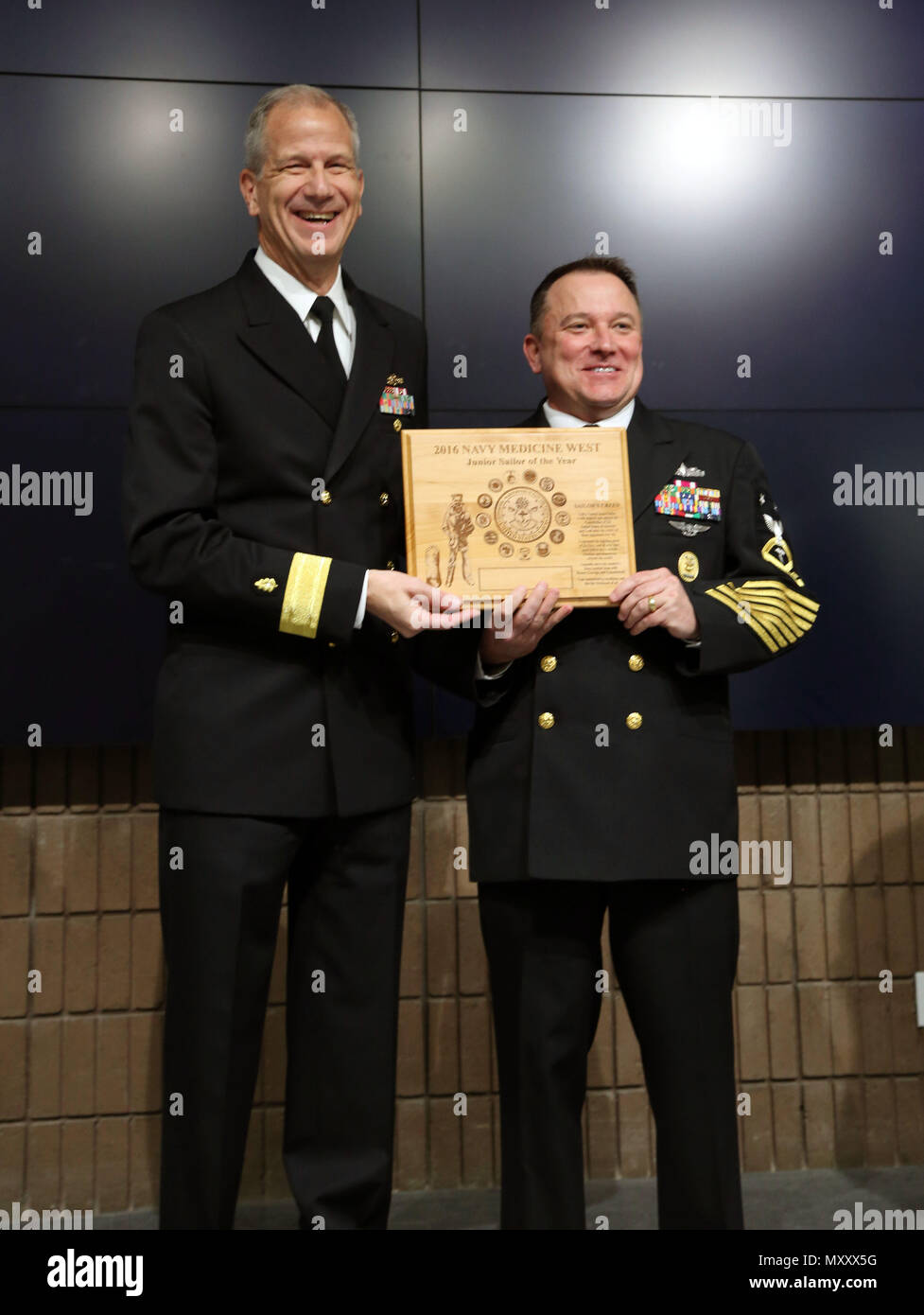 161209-N-KR391-002 SAN DIEGO (Dec 9, 2016) Master Chief Petty Officer Jeffrey Dell, Command Master Chief, Naval Hospital Oak Harbor, receives a plaque for the Navy Medicine West Junior Sailor of the Year on behalf of Petty Officer 2nd Class Christopher Hough, from Naval Hospital Oak Harbor, in an auditorium packed with Sailors and civilians at Navy Medicine West headquarters.  Rear Adm. Paul Pearigen, Commander Navy Medicine West (left) presented the plaque.  (Photo by Chief Petty Officer Kimberley Blaine-Sweet /Released) Stock Photo