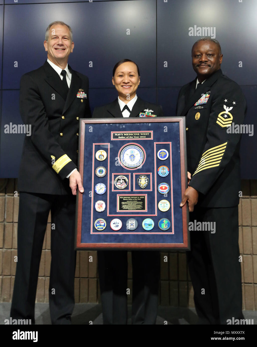 161209-N-KR391-003 SAN DIEGO (Dec 9, 2016) Rear Adm. Paul Pearigen, Commander Navy Medicine West (left), and Master Chief Hosea Smith, Command Master Chief, Navy Medicine West (right), present the Navy Medicine West Sailor of the Year plaque to Petty Officer 1st Class Tiffany Kidd, from U.S. Naval Hospital Yokosuka, in an auditorium packed with Sailors and civilians at Navy Medicine West Headquarters. (Photo by Chief Petty Officer Kimberley Blaine-Sweet /Released) Stock Photo