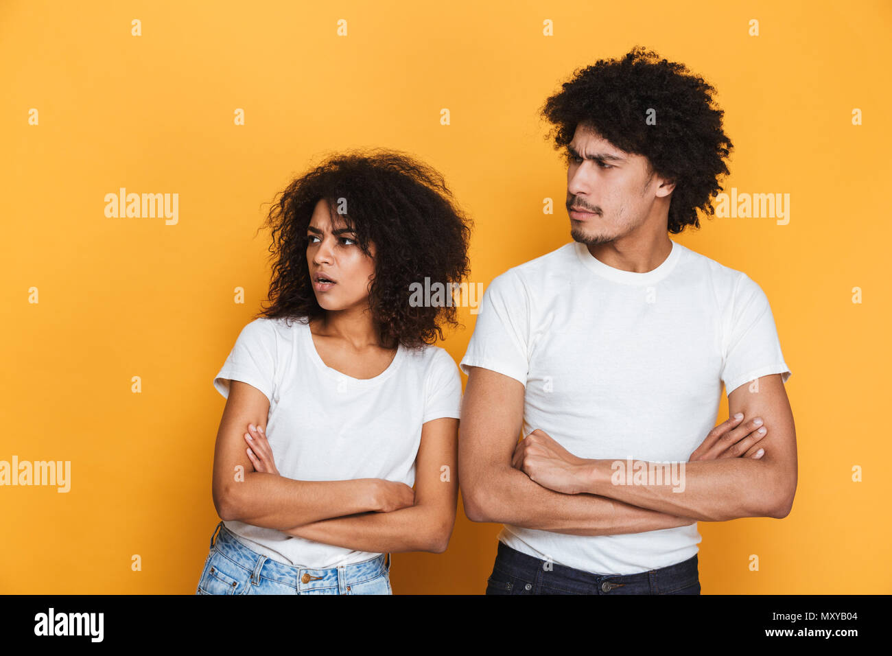 Portrait of an upset young afro american couple standing with arms folded and looking away isolated over yellow background Stock Photo