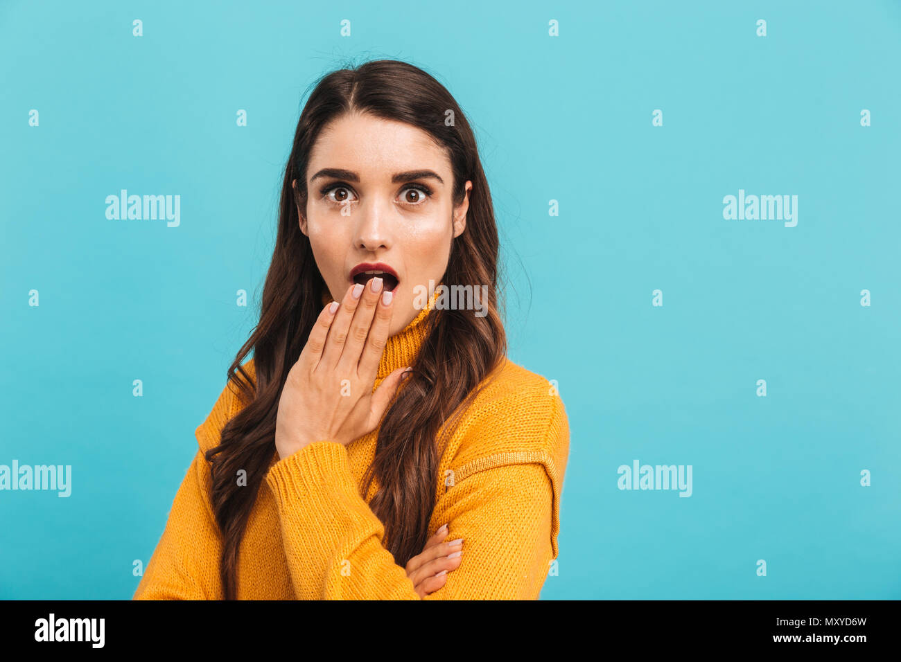 Portrait of a shocked miling young girl in sweater covering mouth with hand isolated over blue background Stock Photo