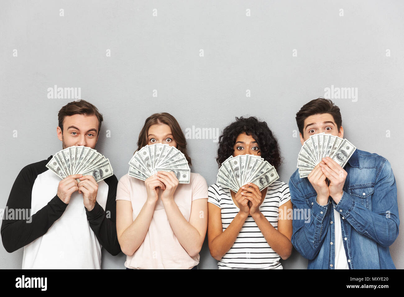 Image of emotionl group of friends standing isolated over grey wall background looking camera holding money covering faces. Stock Photo