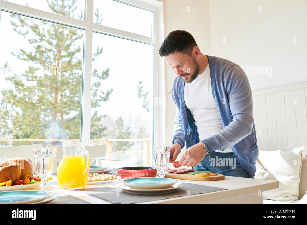 Side view portrait of mature bearded man setting dinner table while