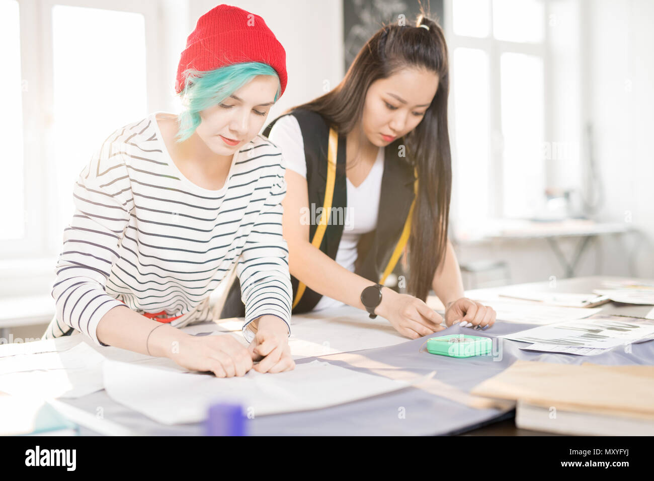 Portrait of two contemporary young women making patterns for custom made clothes on tailors table while collaborating on creative fashion design proje Stock Photo