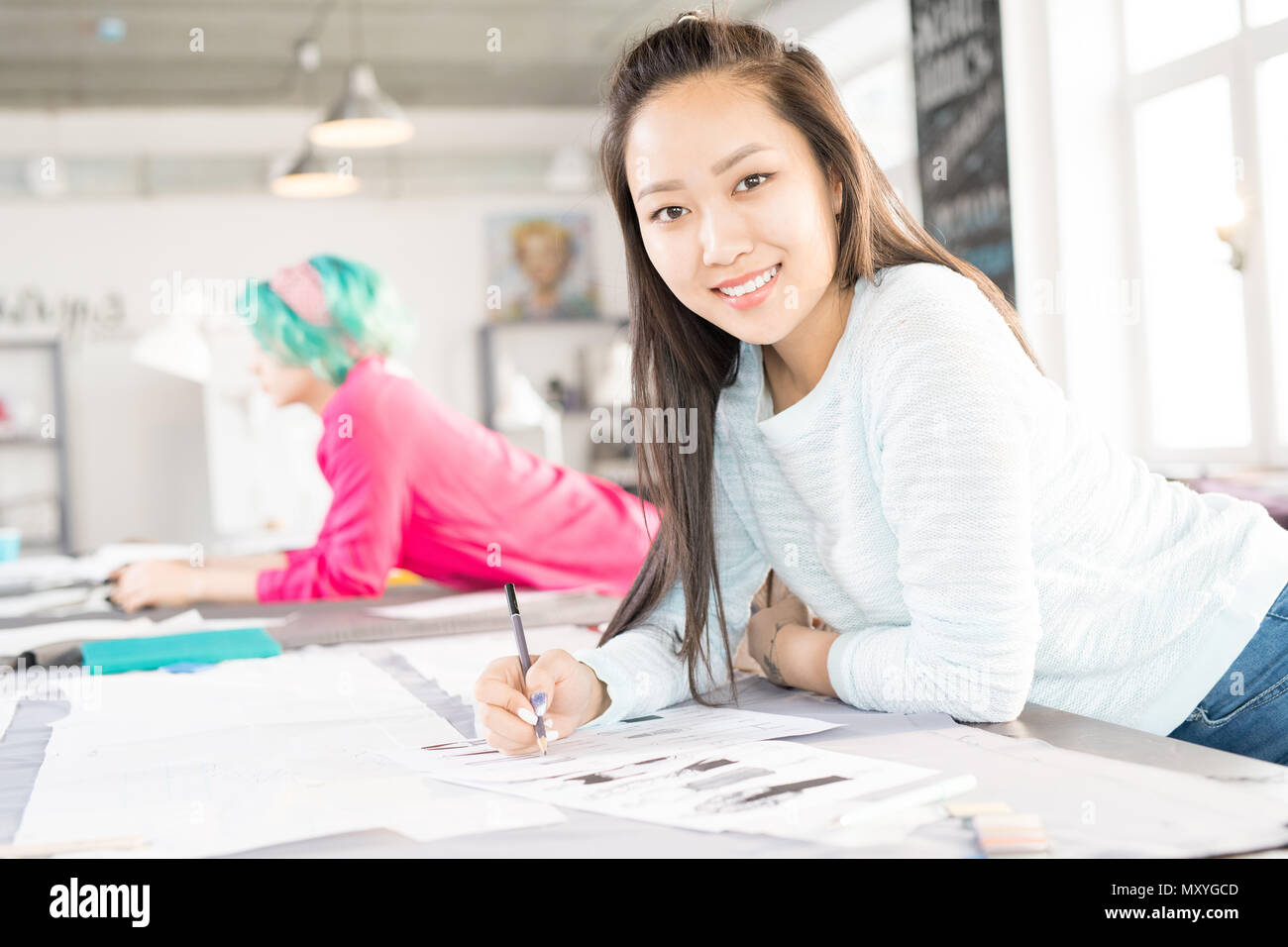 Portrait of smiling Asian woman looking at camera while drawing ...