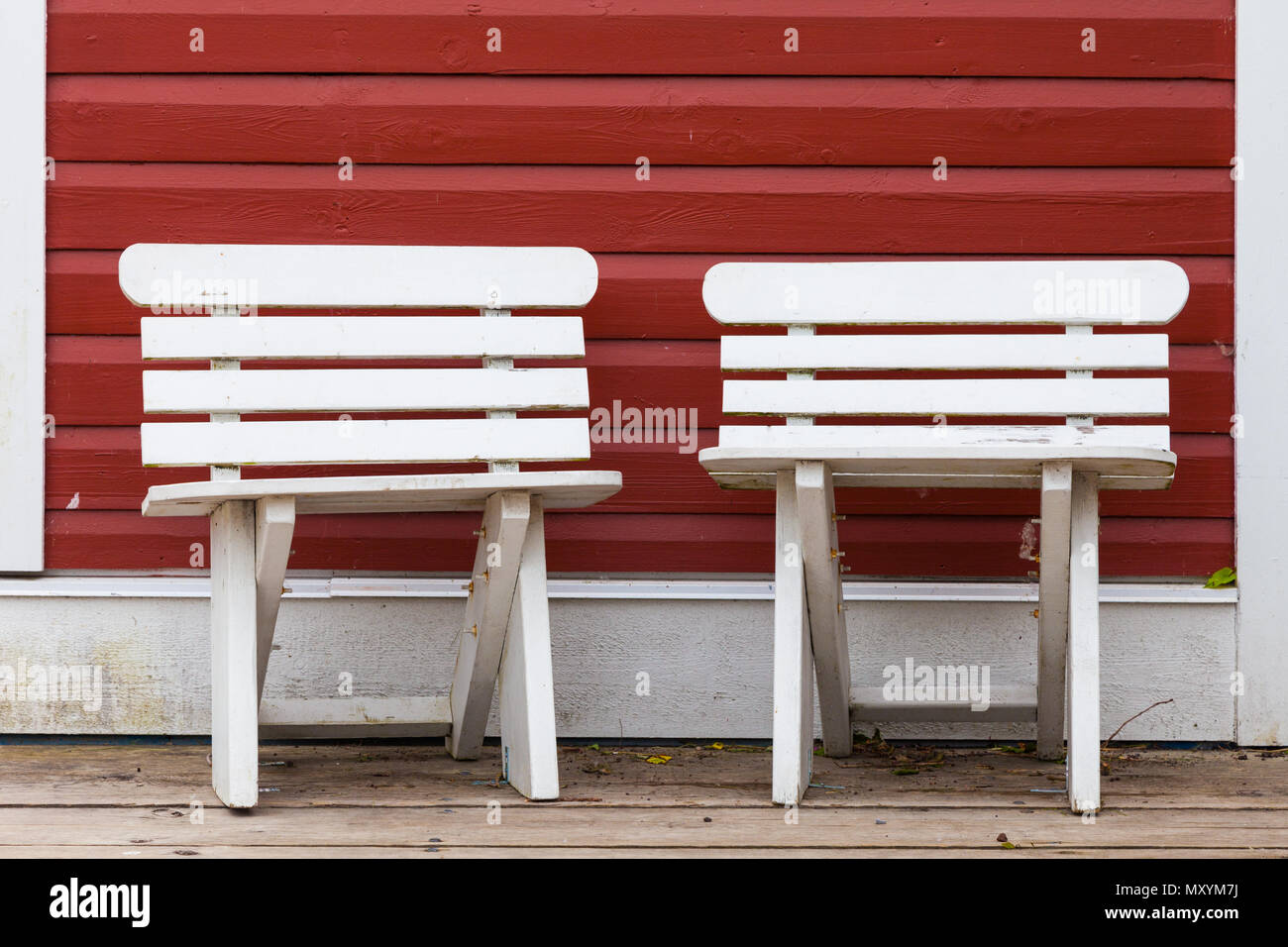 Two small white benches against a red painted wooden wall in Steveston, Canada Stock Photo