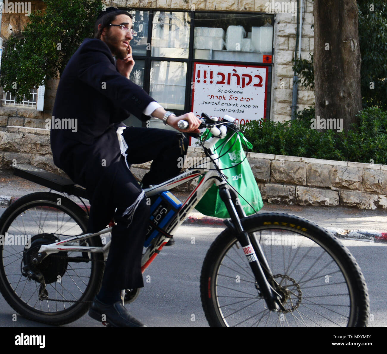 A Hasidic man talking on his mobile phone as he cycles. Stock Photo