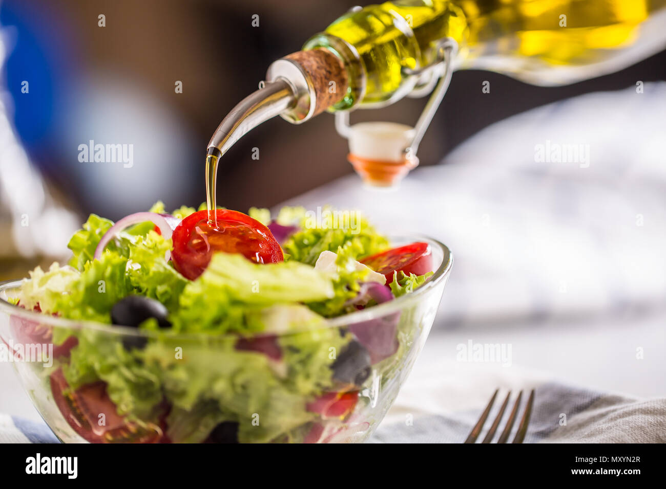 Olive oil pouring into bowl of fresh vegetable salad. Stock Photo