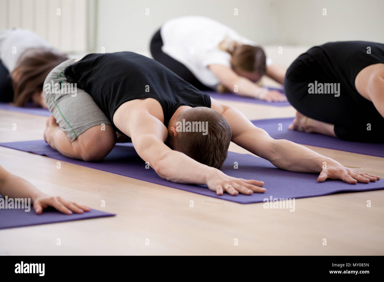 Group of young sporty people practicing yoga lesson, doing Child exercise, resting in Balasana pose, working out, indoor studio session close up, stud Stock Photo