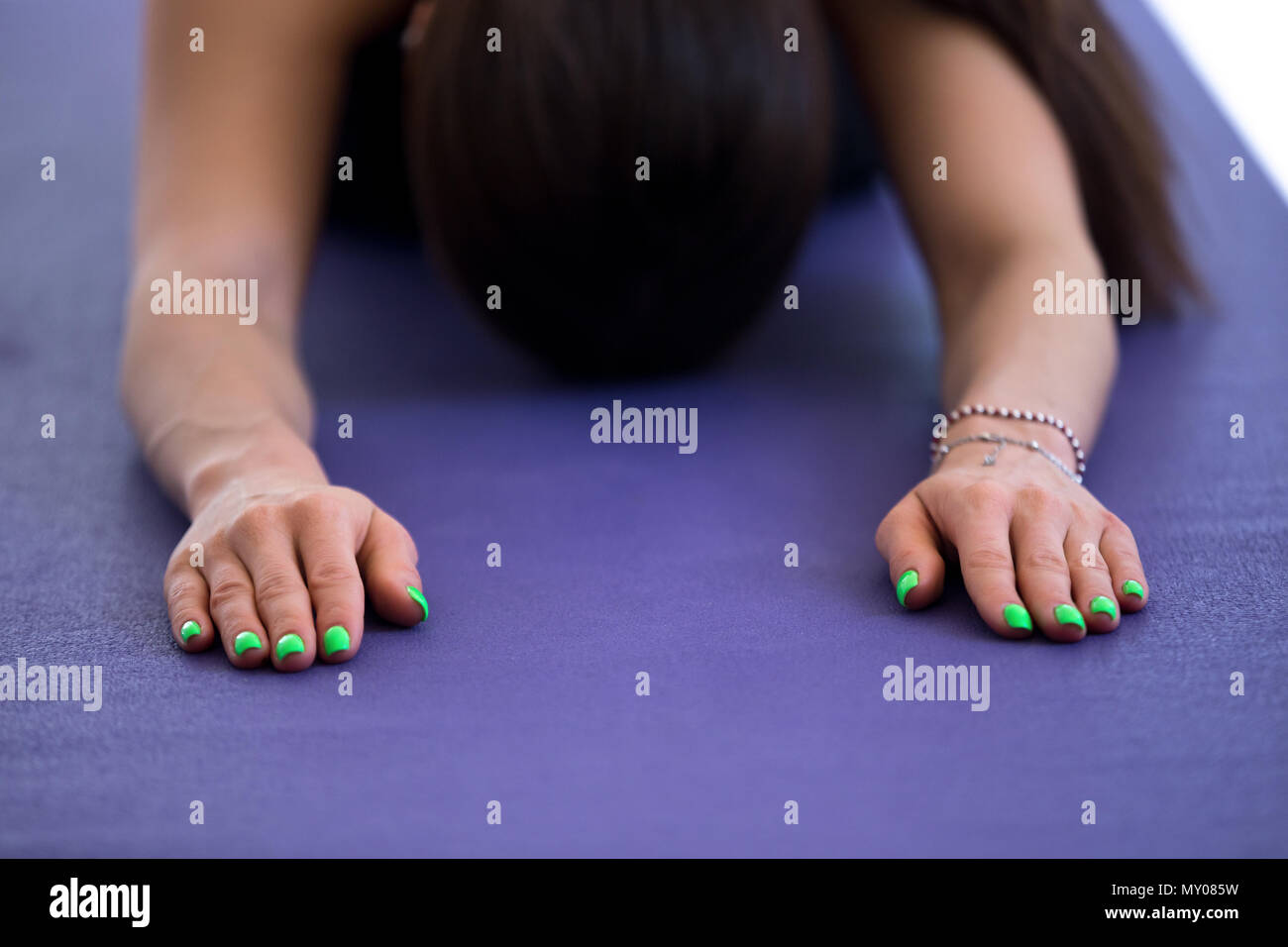 Female laying hands with spring green manicure on the floor, practicing yoga, doing Child exercise on purple mat, resting in Balasana pose, working ou Stock Photo