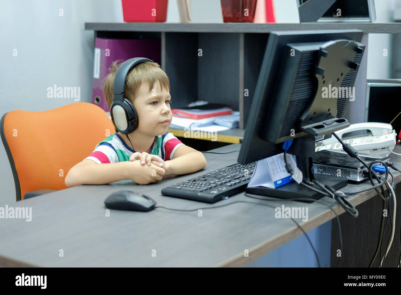 Little boy with headphones sitting at computer in office Stock Photo