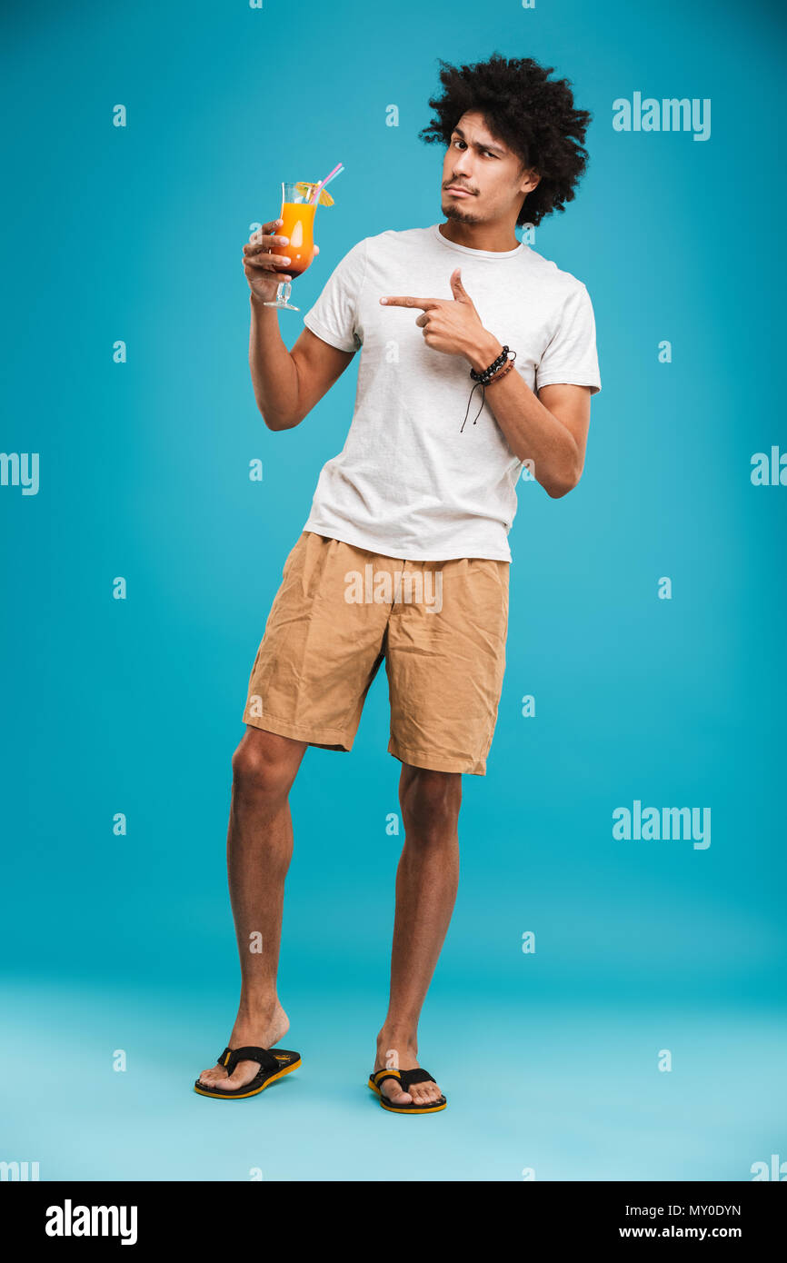 Image of handsome young african curly man standing isolated over blue background holding cocktail pointing. Stock Photo