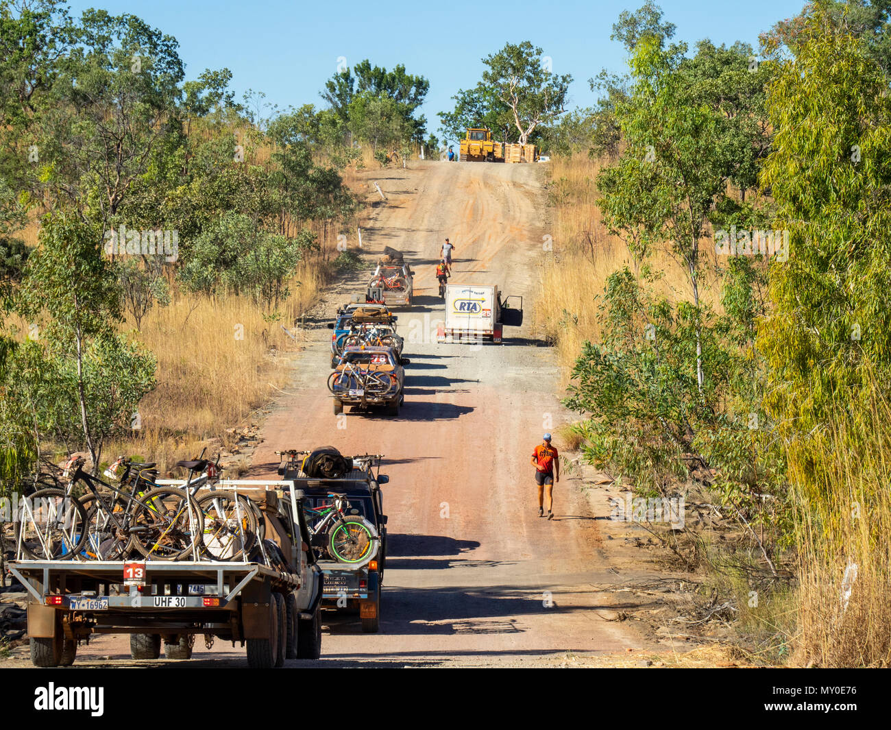 Two cyclists riding past a convoy of four wheel drive vehicles and up a hill in the Gibb Challenge 2018 on the Gibb River Road Kimberley WA Australia Stock Photo