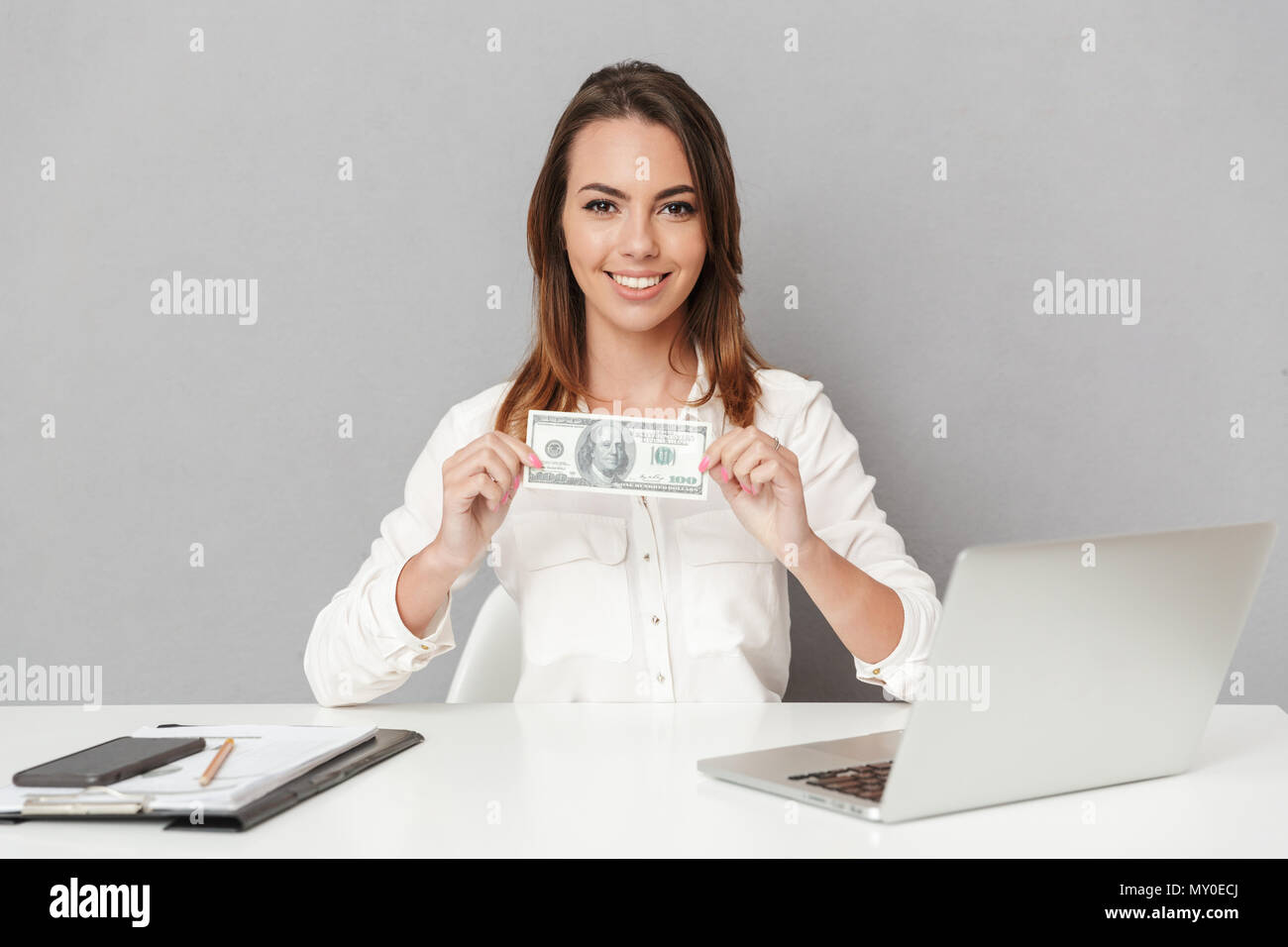 Portrait of a happy young business woman sitting at the office desk and ...