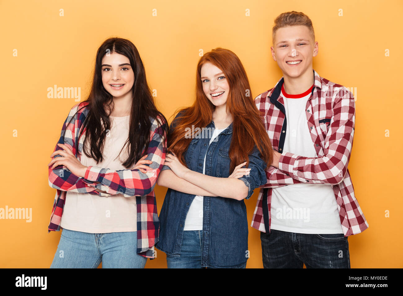 Group of happy school friends standing together with arms folded over yellow background Stock Photo