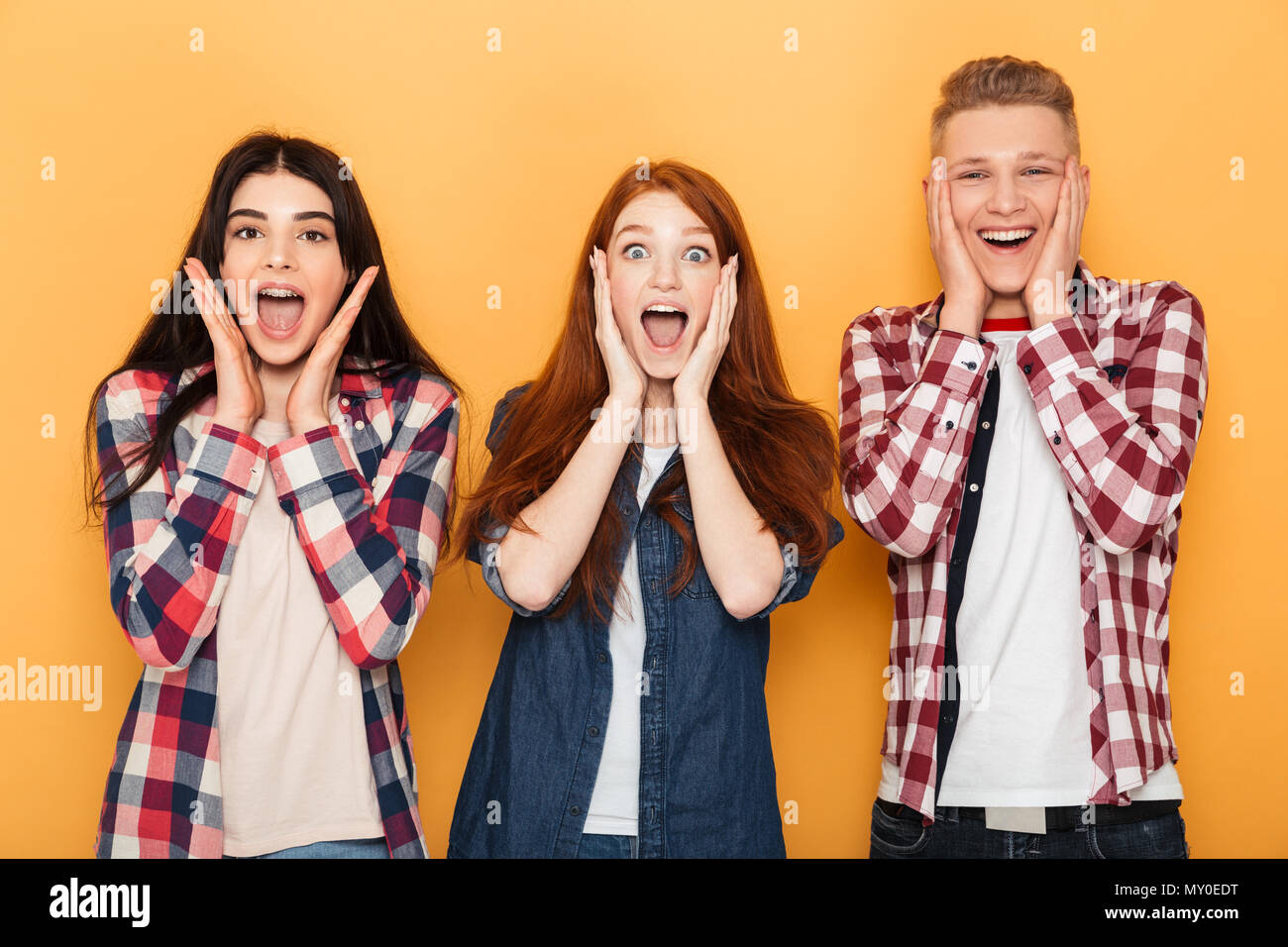 Group of happy school friends screaming while standing together over yellow background Stock Photo