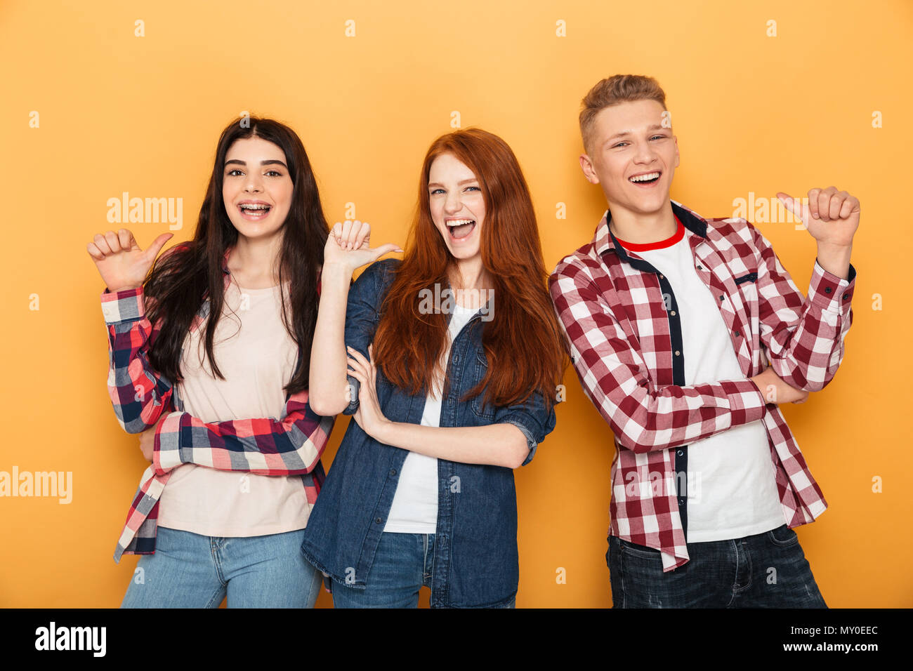 Group of happy school friends pointing fingers at themselves while standing together over yellow background Stock Photo