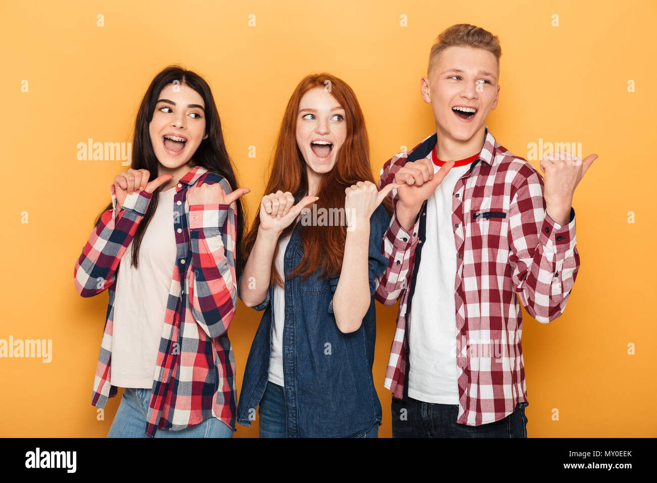 Group of happy school friends pointing fingers away at copy space while standing together over yellow background Stock Photo