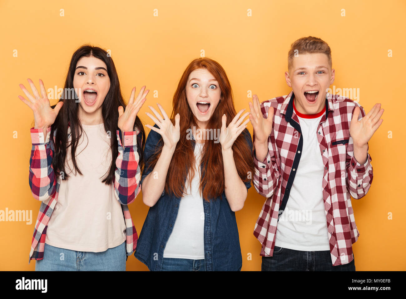 Group of surprised school friends screaming while standing together over yellow background Stock Photo