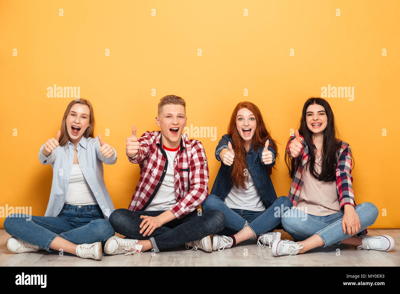 Group of young positive school friends sitting and showing thumbs up ...