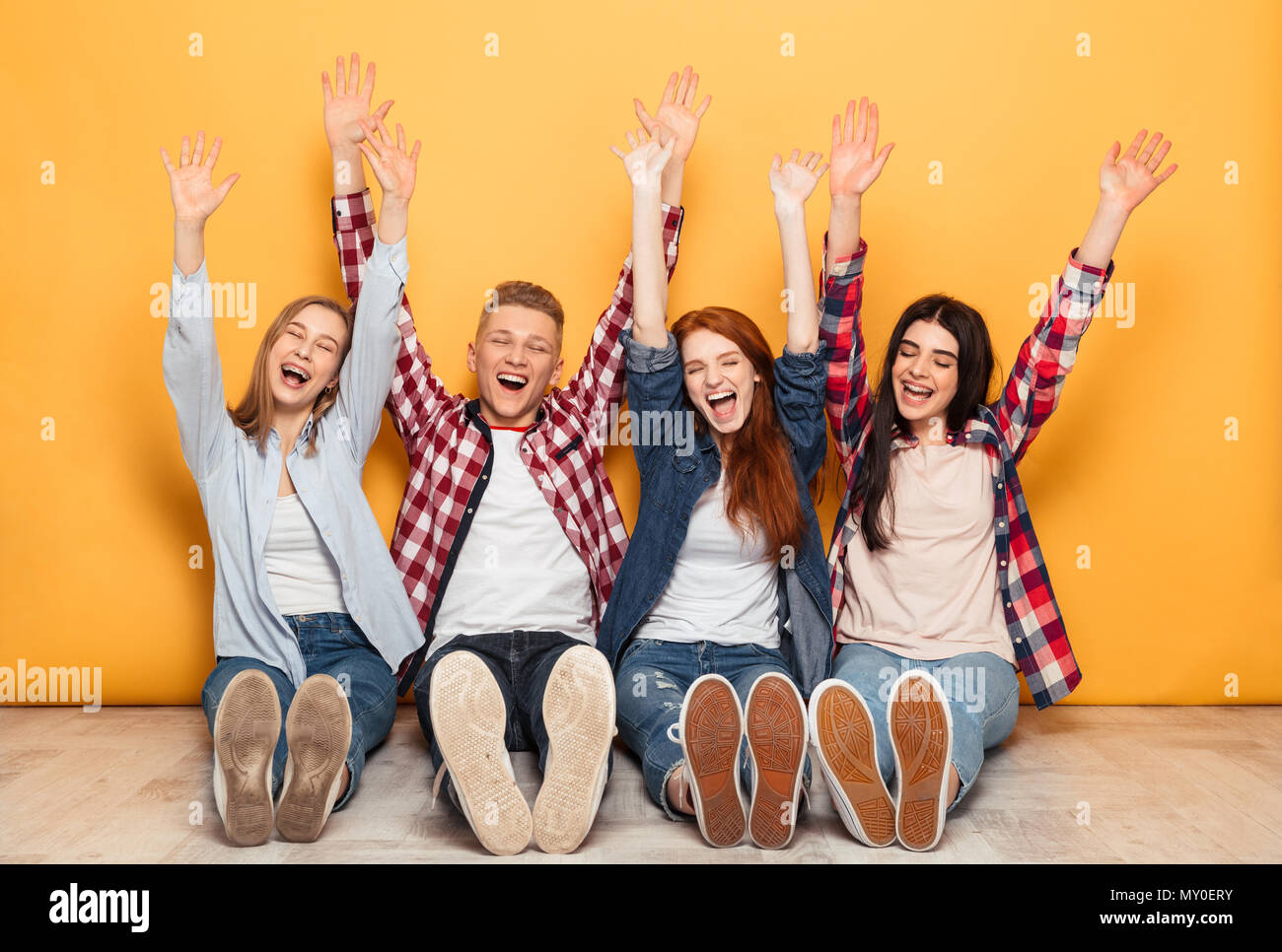 Group of young positive school friends sitting with hands raised over ...