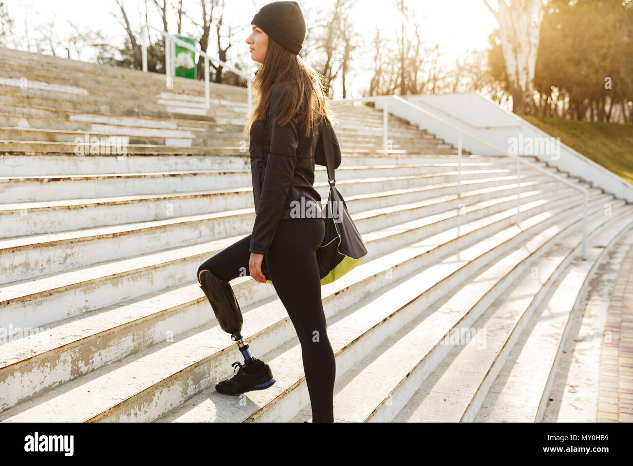 Image of disabled running girl with prosthetic leg in sportswear walking up the stairs in street