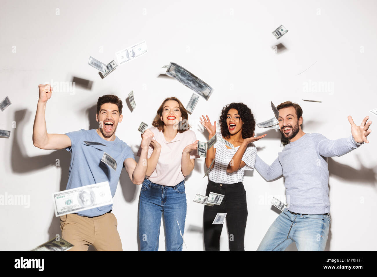 Group of happy multiracial people standing under money banknotes shower and celebrating isolated over white background Stock Photo